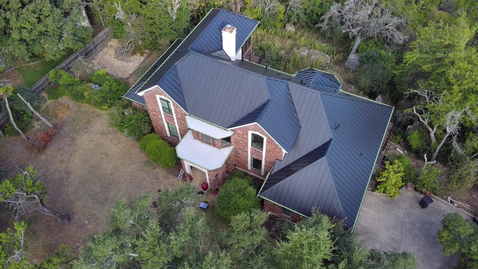 Aerial view of a dark standing seam metal roof installed by Superior on a brick home in the Texas Hill Country